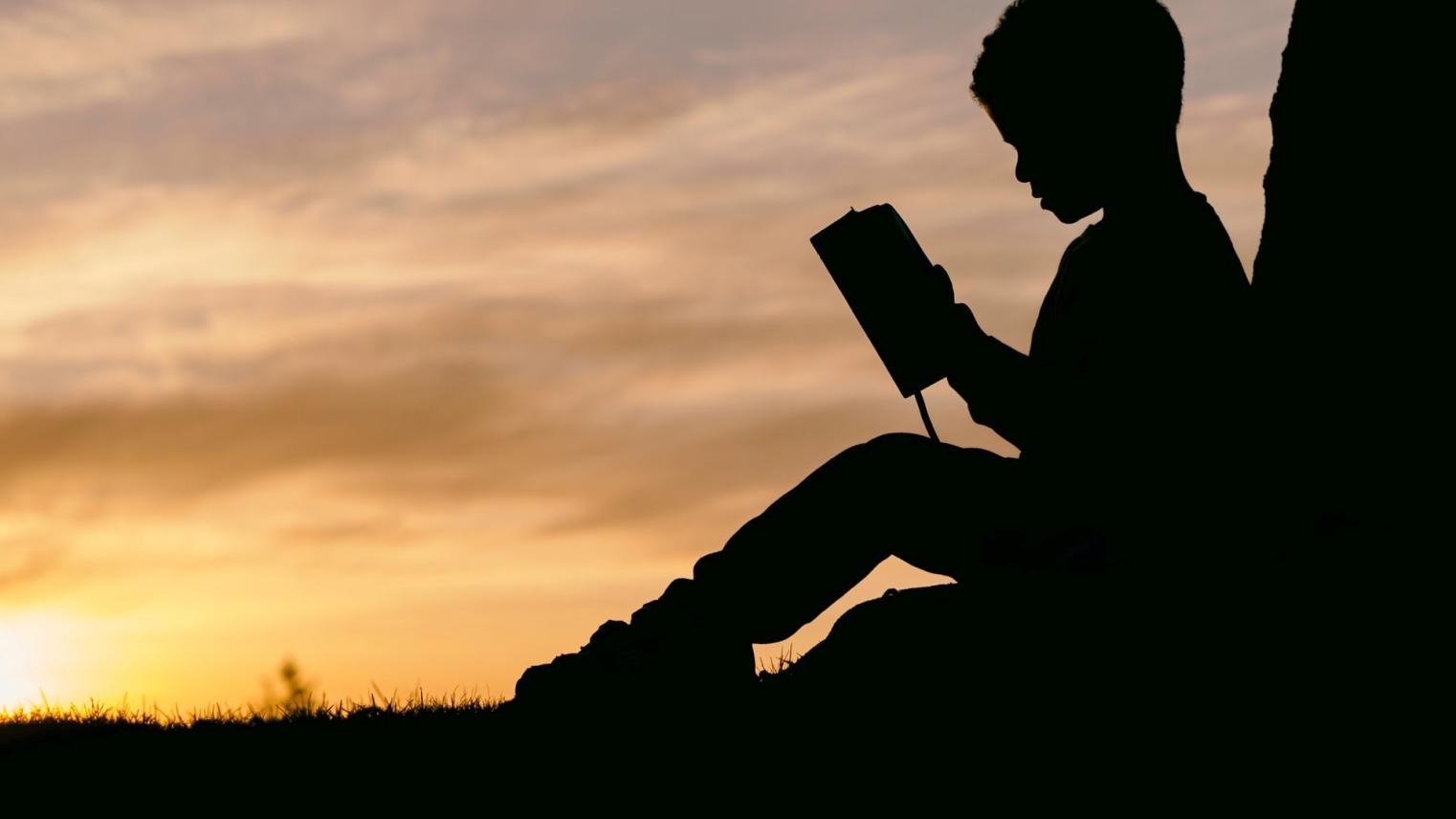 Silhoette of a boy reading a book