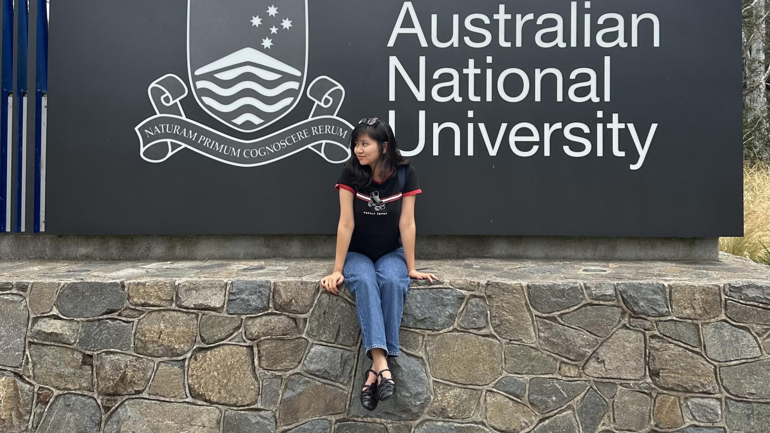 International postgraduate student Binh Thanh Ho International postgraduate student Binh Thanh Ho sitting on a stone wall in front of a sign for the Australian National University