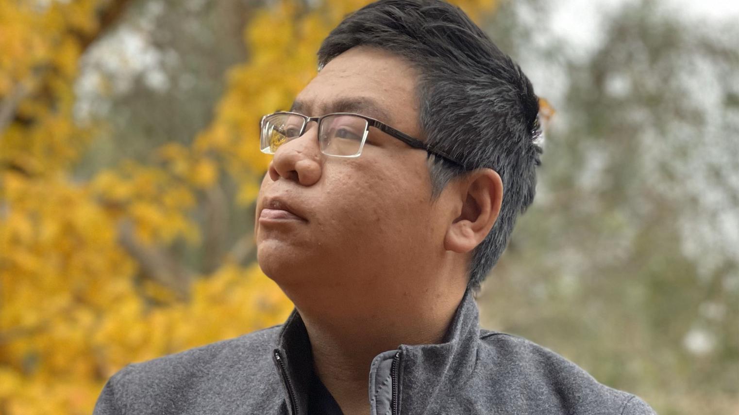 Minh Nguyen Thanh sitting on a wall in front of a sign for the Australian National University